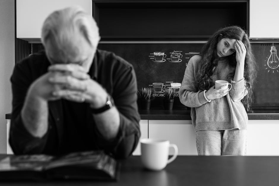A man and woman in a kitchen reflect with mugs, conveying emotions.