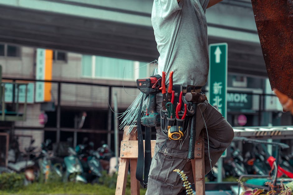 Handyman standing on a ladder with tool belt, repairing outdoors with visible to