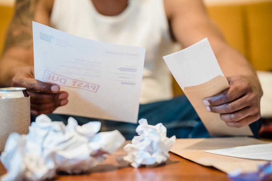Man sitting indoors reviewing past due bills with crumpled papers on a coffee ta