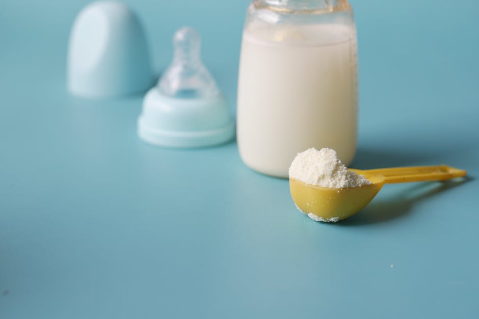 Close-up of baby milk formula powder in a yellow scoop with a bottle on a blue b