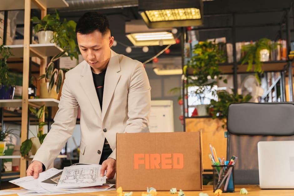 An employee packing documents into a box labeled 'FIRED' in an office environmen
