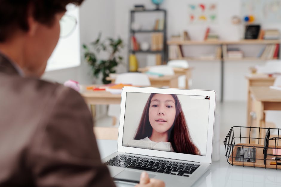Teacher using laptop for virtual lesson with female student on screen in classro