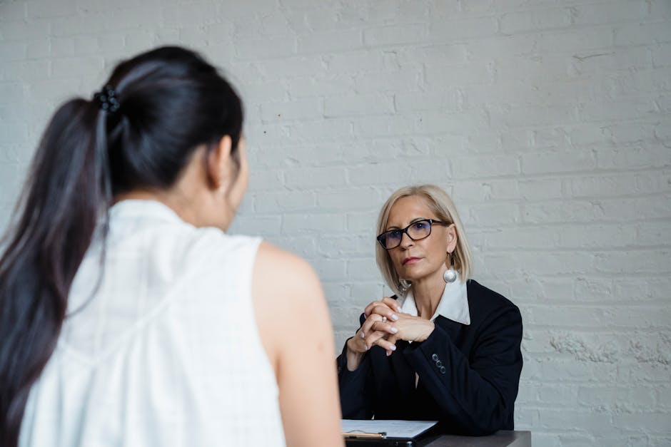 Two women having a serious conversation in an office setting against a brick wal