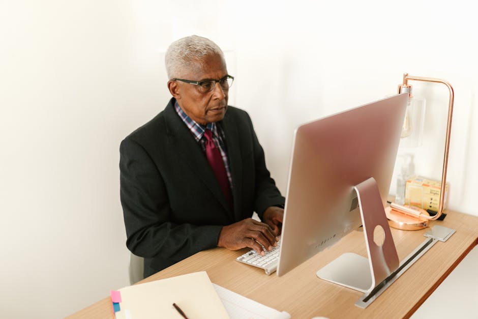 Senior man in corporate attire focusing on work at his desktop computer in a mod