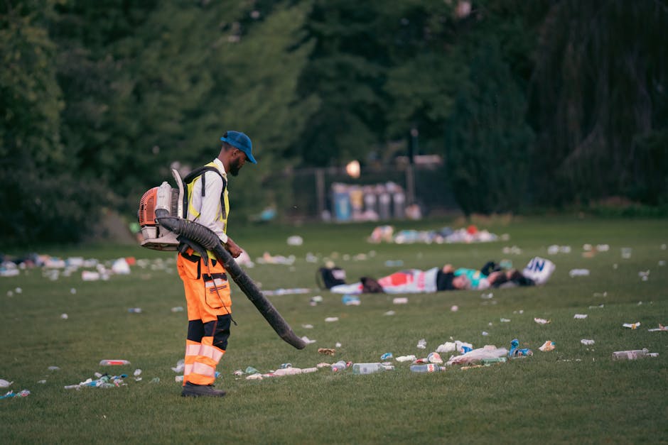 Cleaning staff with leaf blower managing trash in a park after a public event.