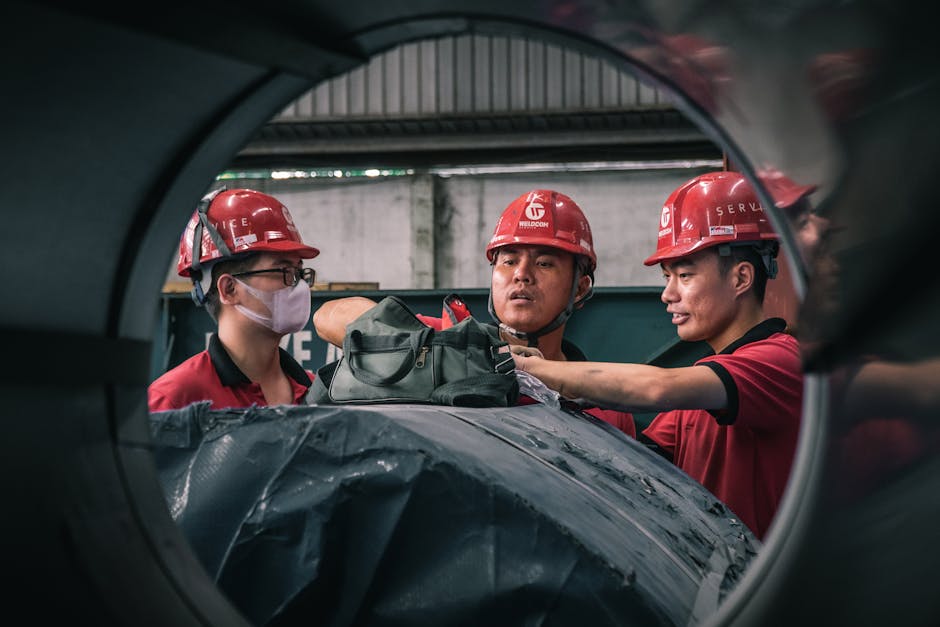 Three workers in safety helmets collaborate inside a factory setting, emphasizin