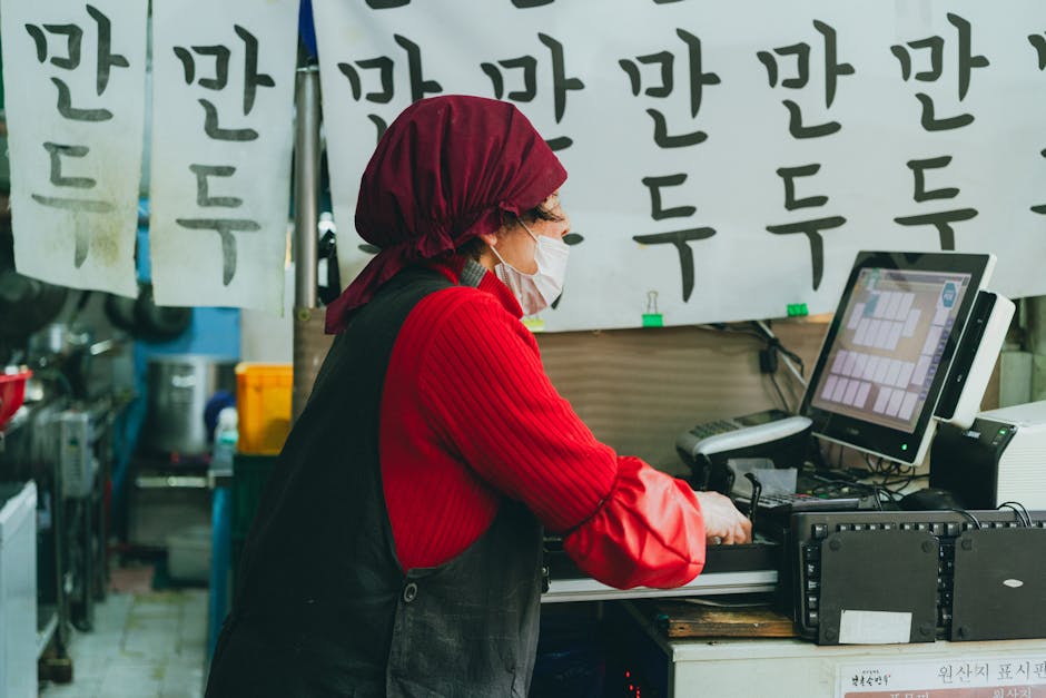 A woman works in a Seoul street market, surrounded by Korean script signs.