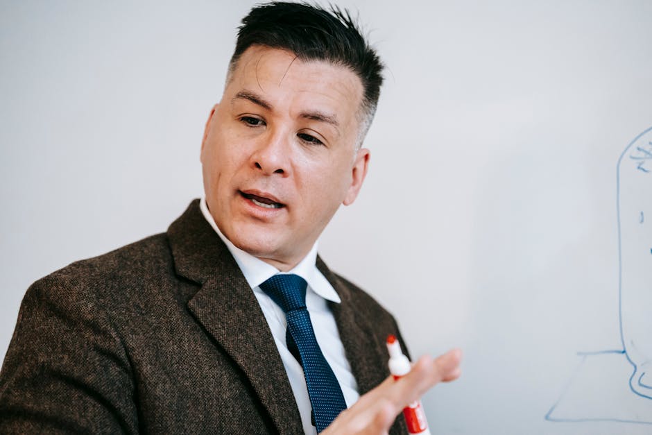 A professional male educator in formal attire using a marker to explain a concep