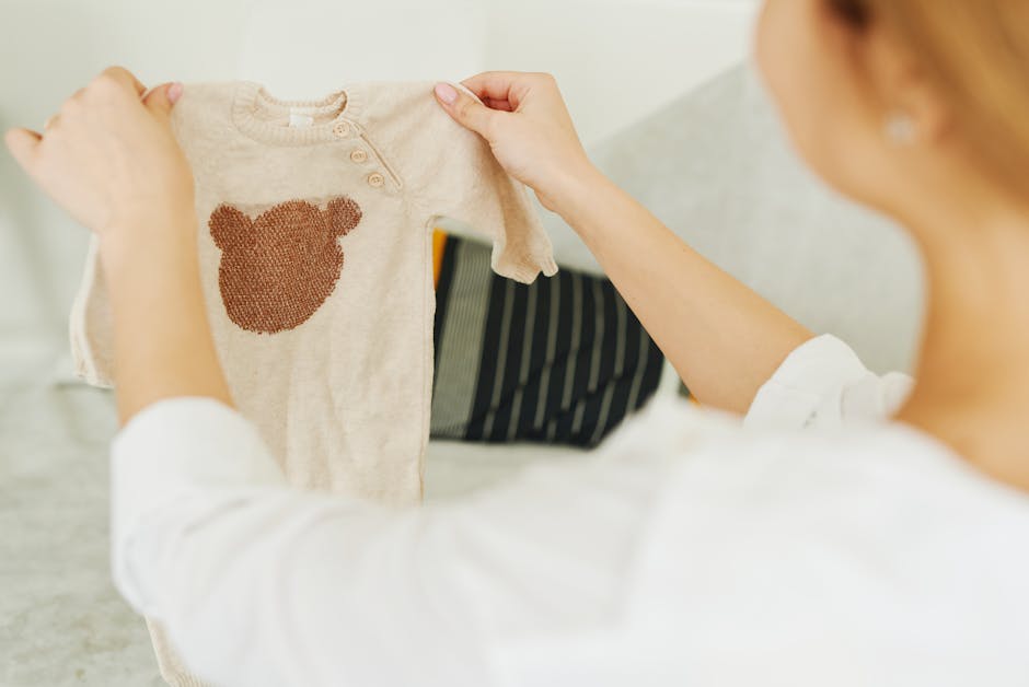 Woman examining a beige baby jumper with a teddy bear design, showcasing cute ba