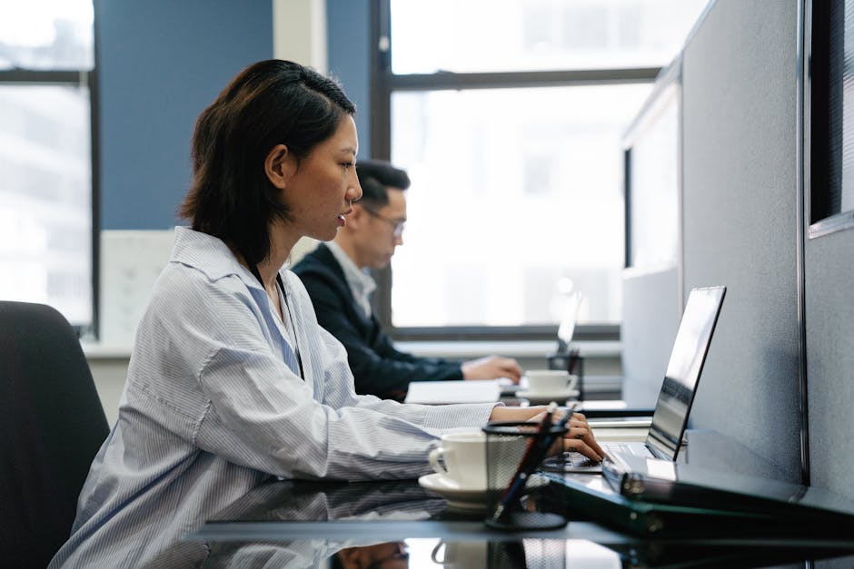 Two professionals working diligently on laptops in a modern office setup, captur