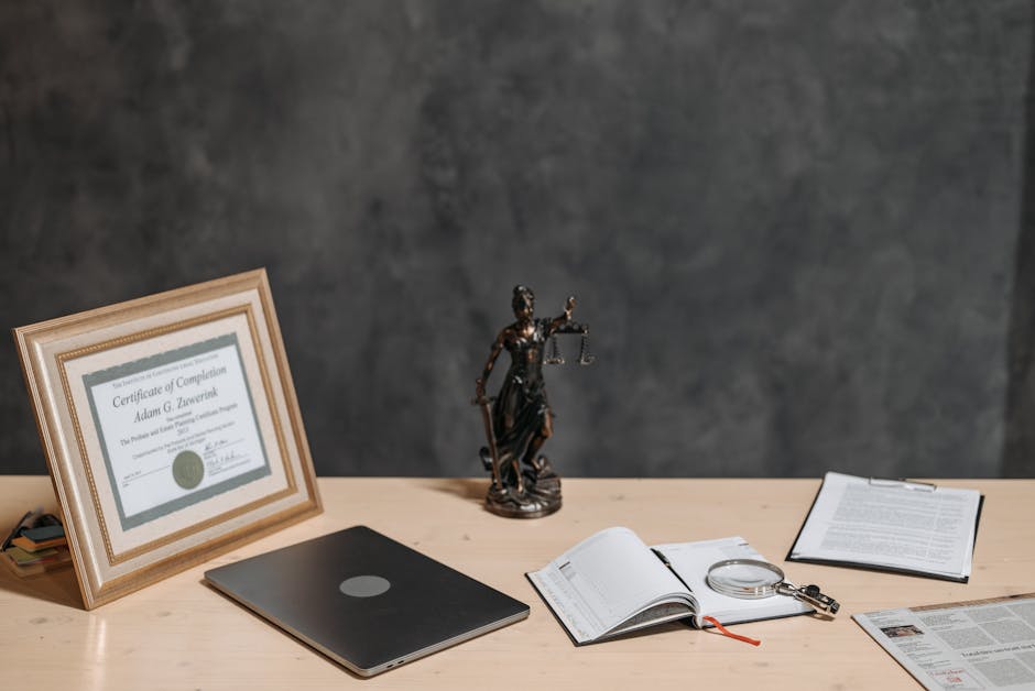 A lawyer's desk featuring a justice statue, diploma, laptop, magnifying glass, a