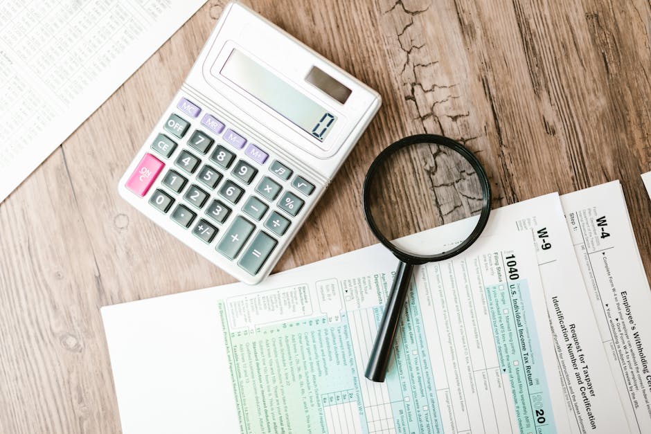 Tax forms laid out with a calculator and magnifying glass on a wooden surface, p