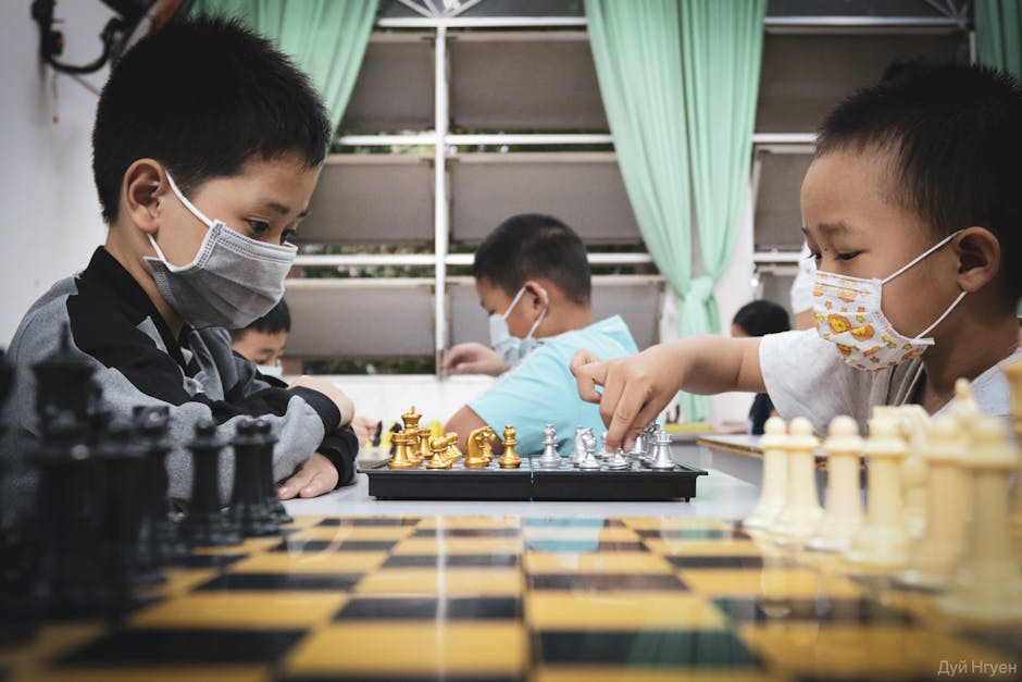Young boys wearing masks intently playing chess in a classroom setting, fosterin