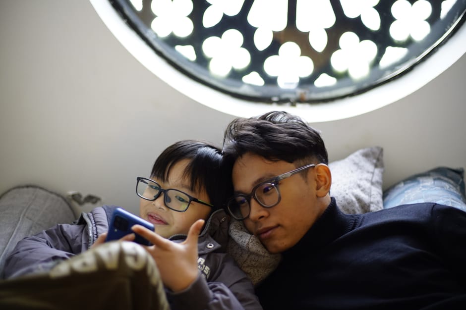 A father and son wearing glasses enjoy a relaxing moment together, using a smart
