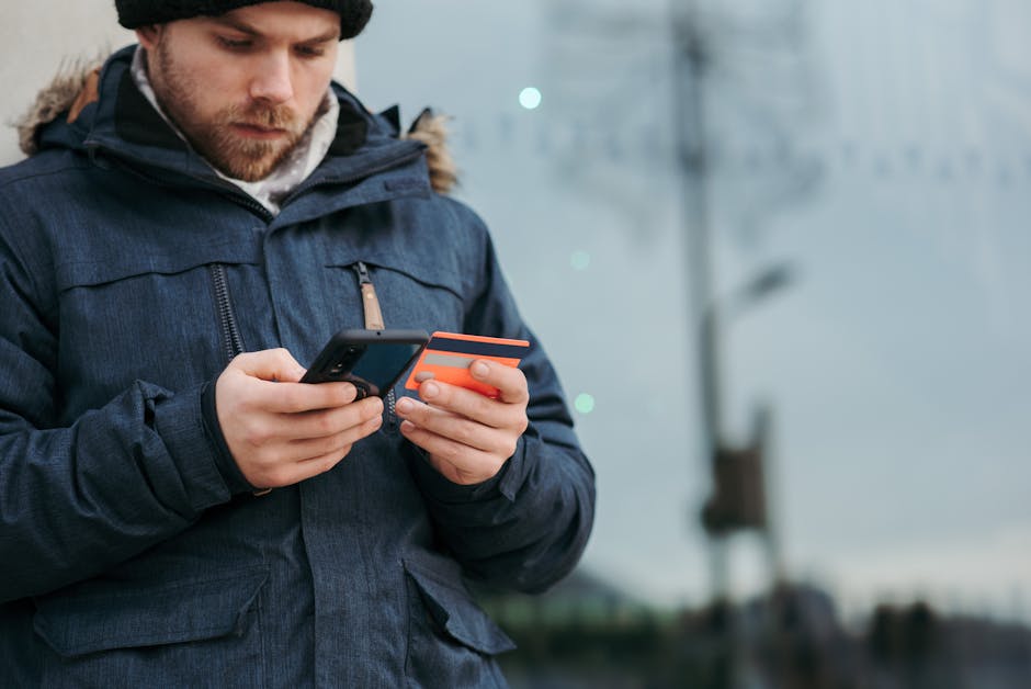 Crop concentrated man in warm clothes entering credentials of credit card on mob